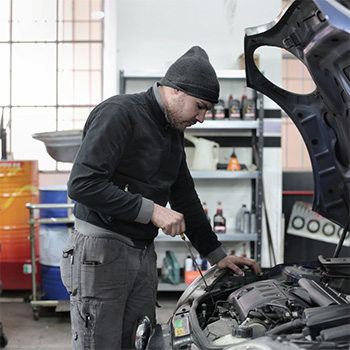 Mechanic wearing a beanie inspecting a car's engine during tune-up service in Safety Harbor, FL